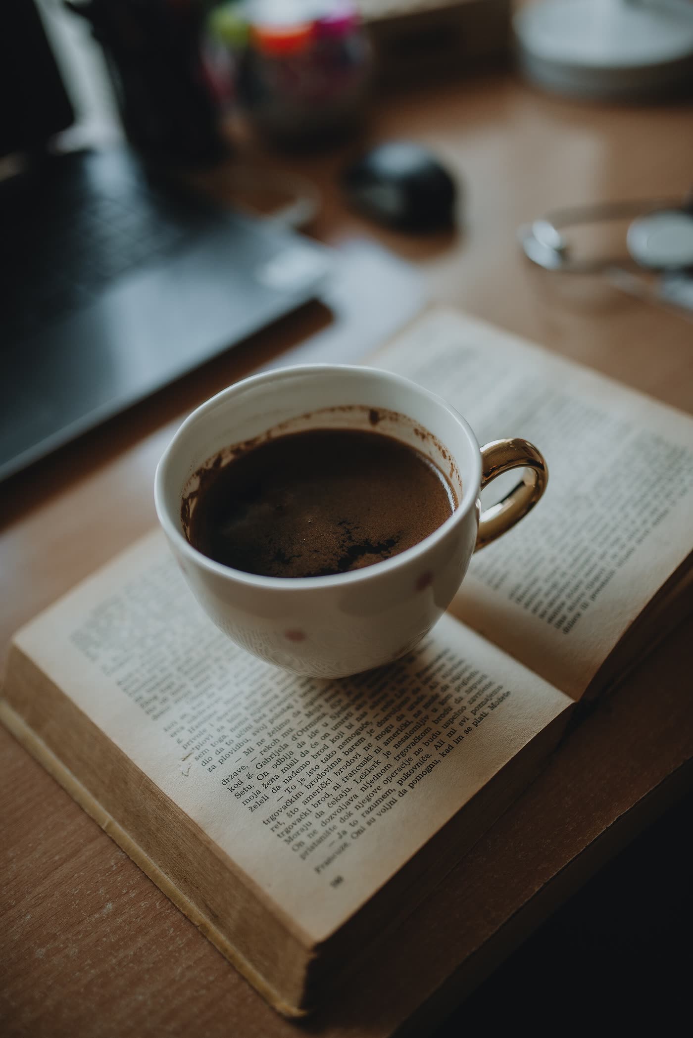 A cup of coffee resting on an open book on a wooden desk