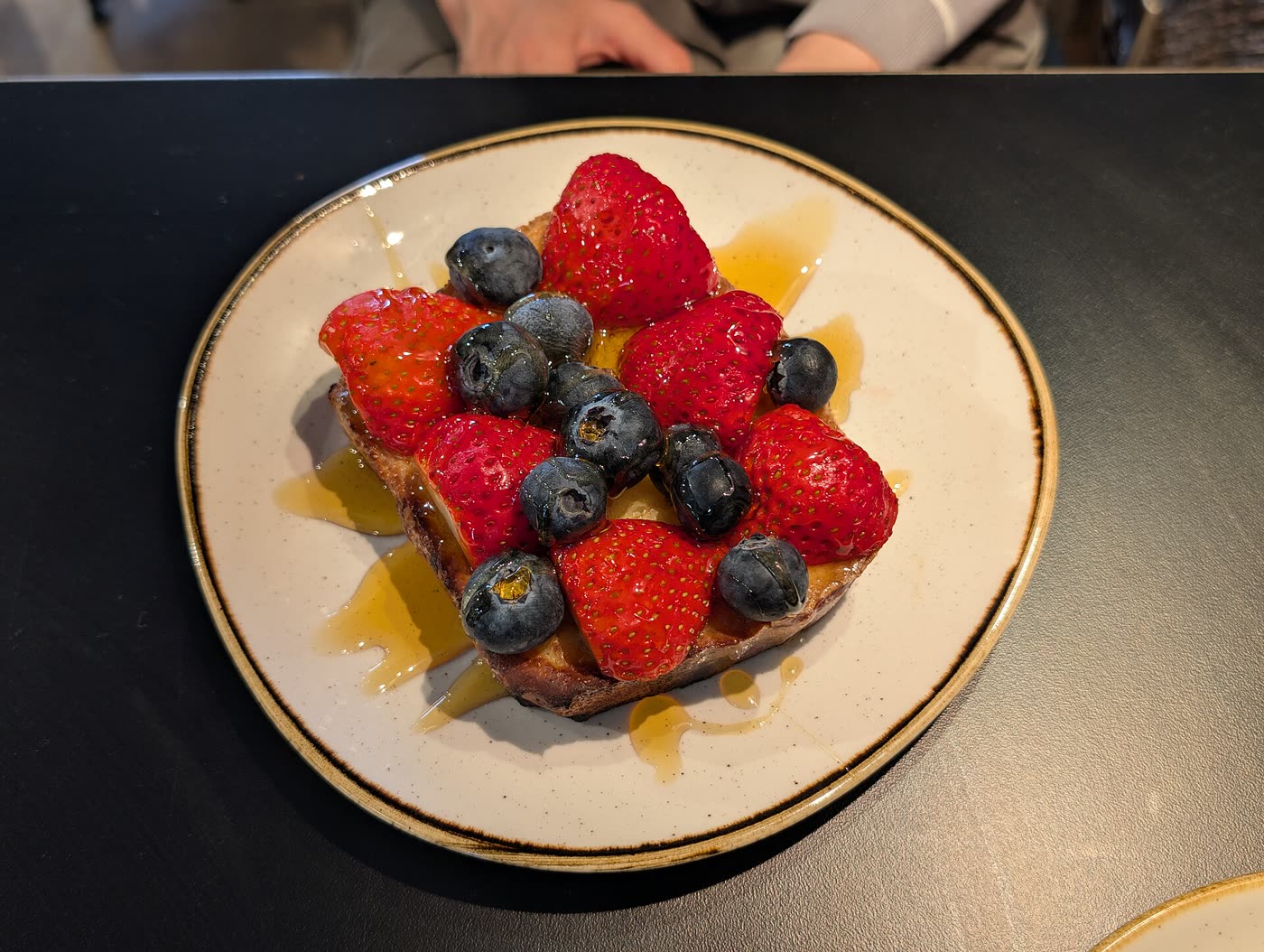 A slice of French toast topped with strawberries and blueberries, drizzled with syrup
