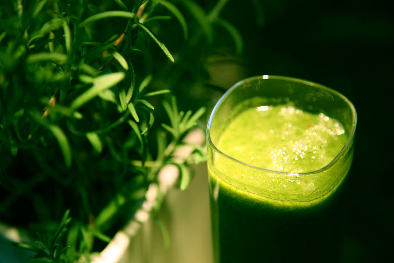 A glass of bright green smoothie beside fresh green herbs